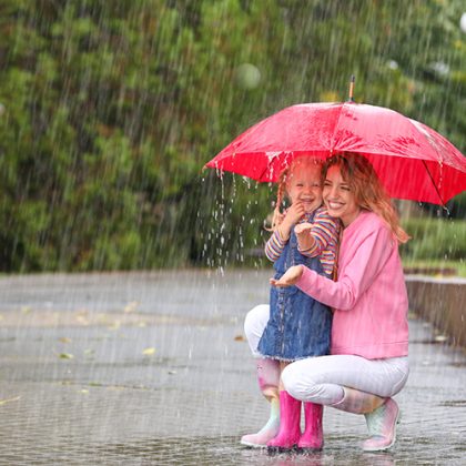 Happy mother and daughter with red umbrella in park on rainy day. Space for text